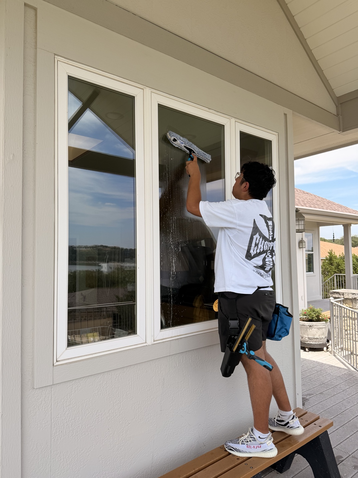 Precise Panes technician hand-cleaning glass with a professional squeegee and BOAB belt on a Lake Travis home